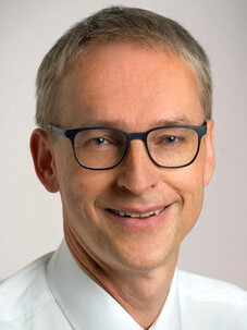 Porträtfoto von Karl Leo mit Brille und weißem Hemd, freundlich lächelnd.